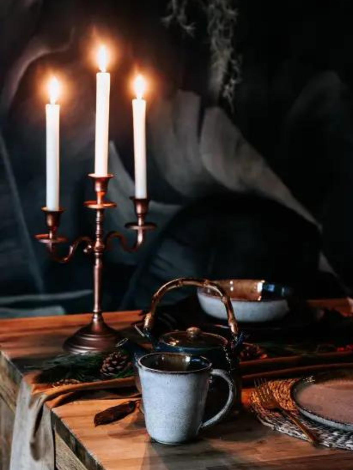 A candleabra and a steaming pot of tea sit on a coffee table.