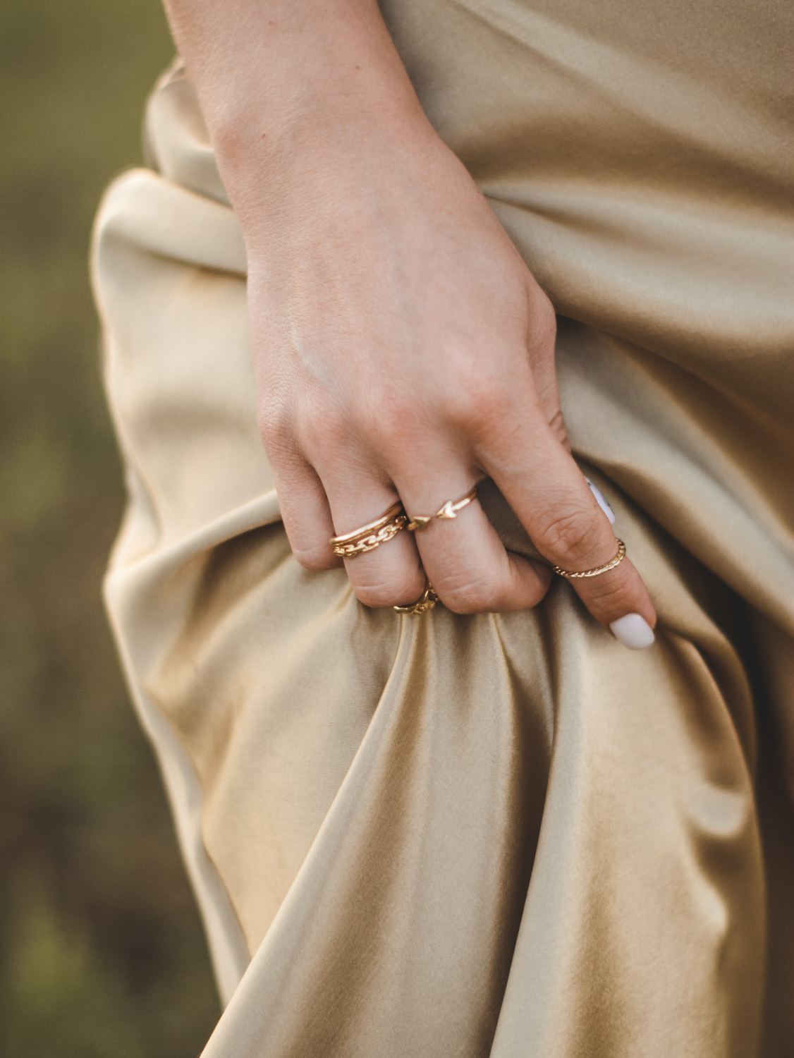 A woman wears a gold satin dress. Her hand gathers the fabric.