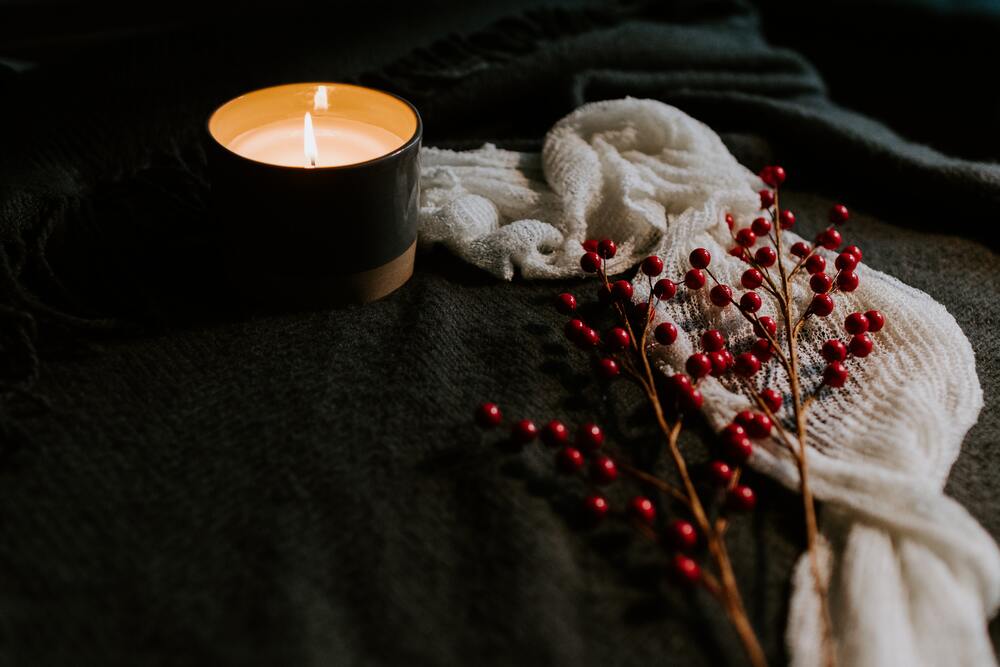 White candle lit on top of a black background and holly berries.